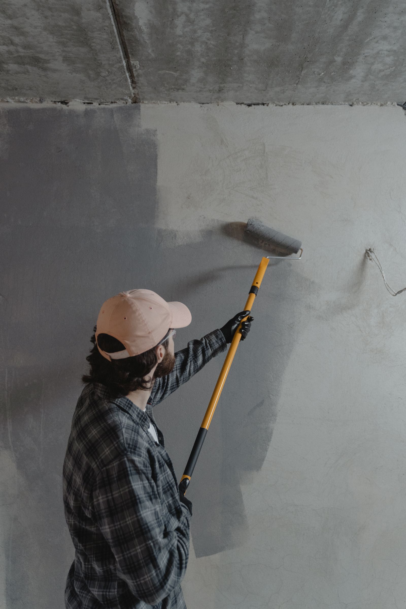 A man using a paint roller to apply gray paint on a wall in an unfinished room — illustrative stock photo, not a photo of Adam or A&A's own work.