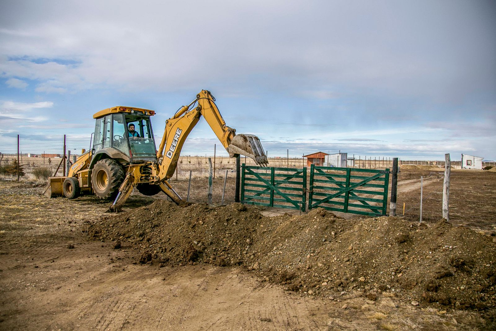 A backhoe digging at a rural Texas farm entrance under a cloudy sky — illustrative stock photo, not Aggieland Septic's own job site.