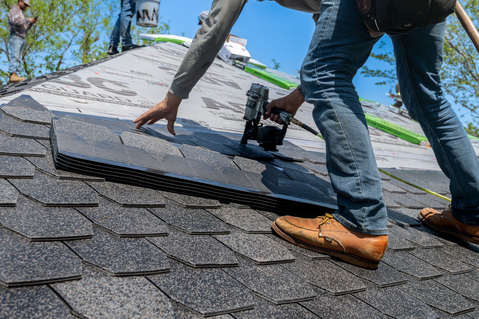 A roofer using a nail gun to install shingles on a residential roof — illustrative stock photo, not a photo of All-Tex Roofing's own crew.