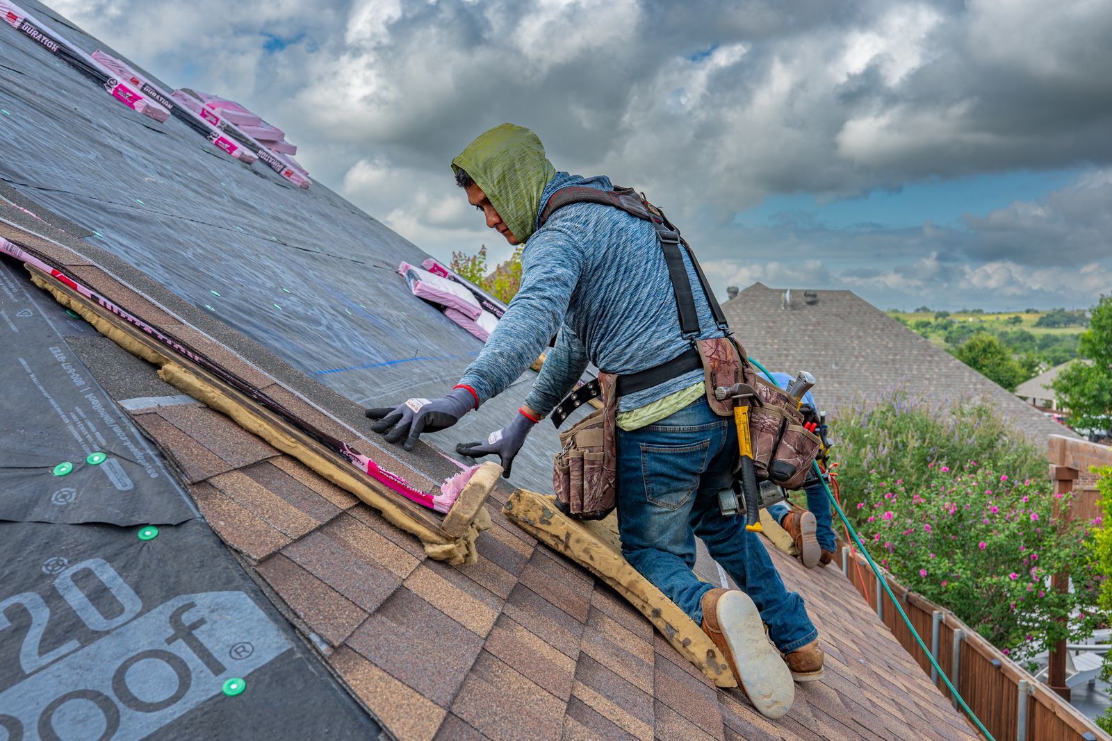 Roofers installing shingles on a home under blue skies — illustrative stock photo, not All-Tex Roofing's own crew.
