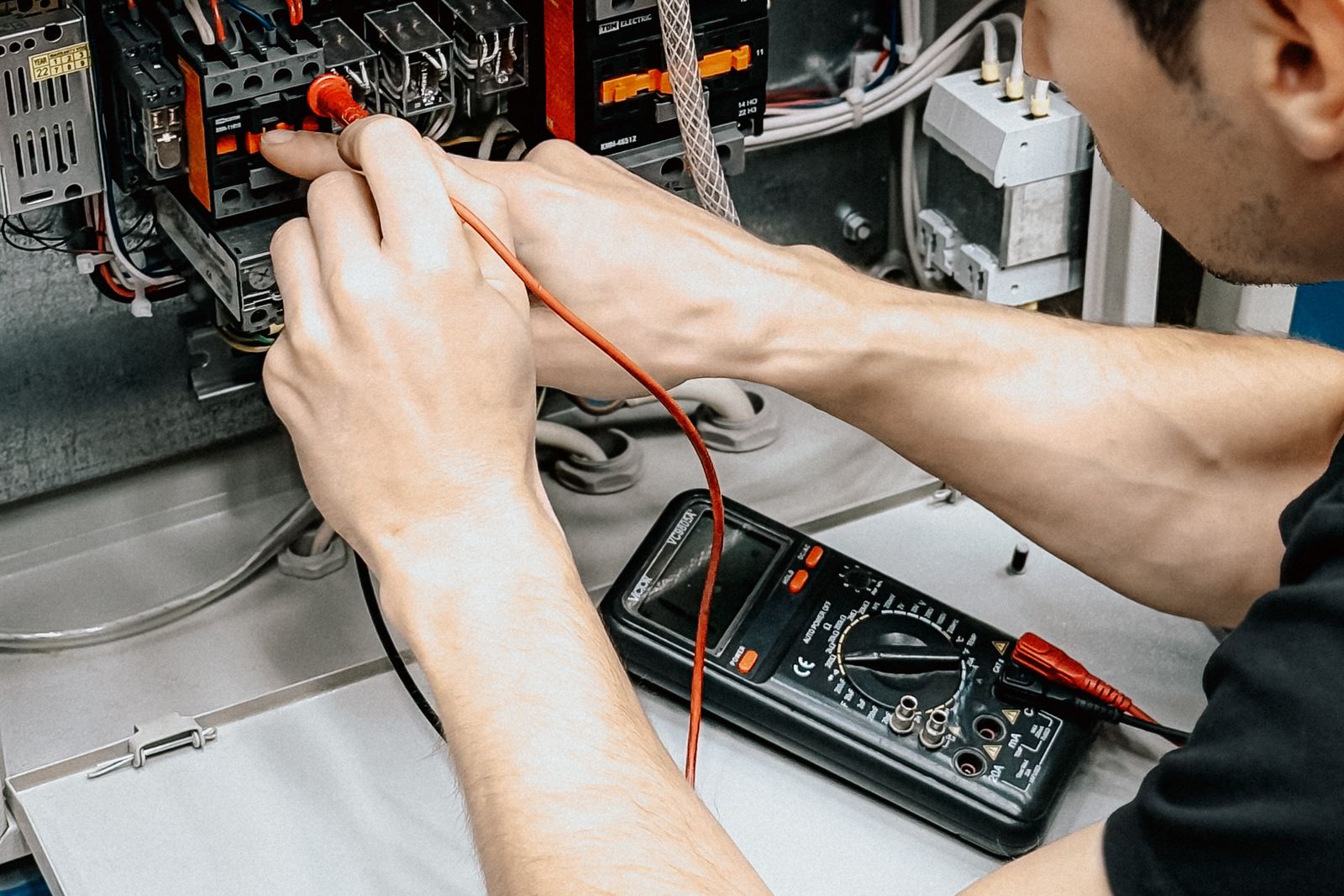 An electrician using a multimeter to diagnose an open electrical panel — illustrative stock photo, not a photo of B&B's own crew.