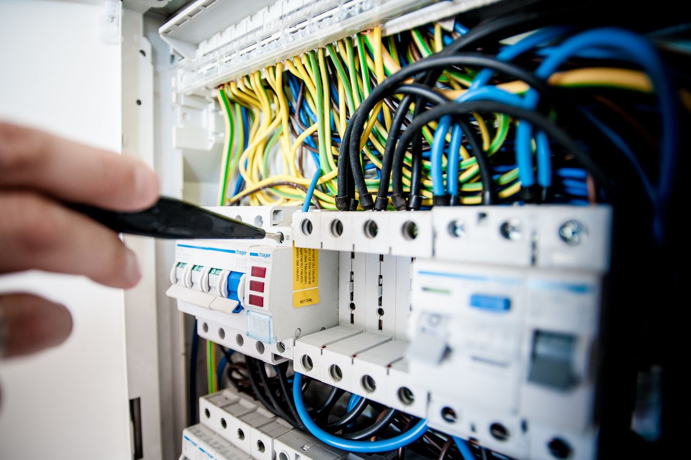 Hand of an electrician working on a circuit breaker panel with colorful wires — illustrative stock photo, not B&B's own panel.