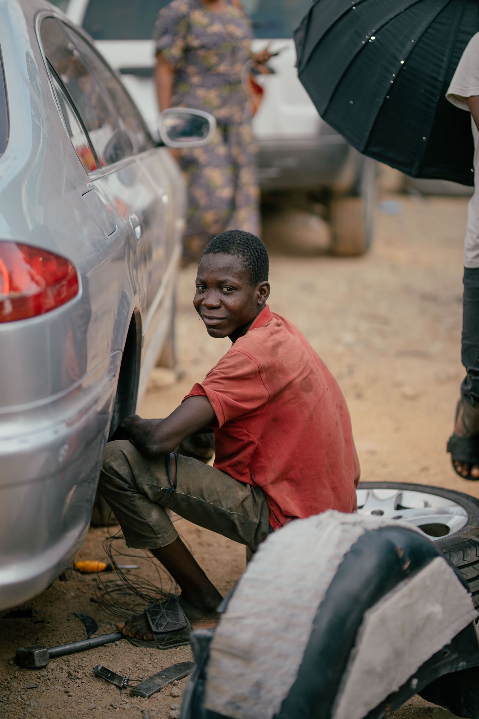 A young mechanic smiling while working on a car tire outdoors — illustrative stock photo, not a photo of Bats Mobile Mechanic or Tony.