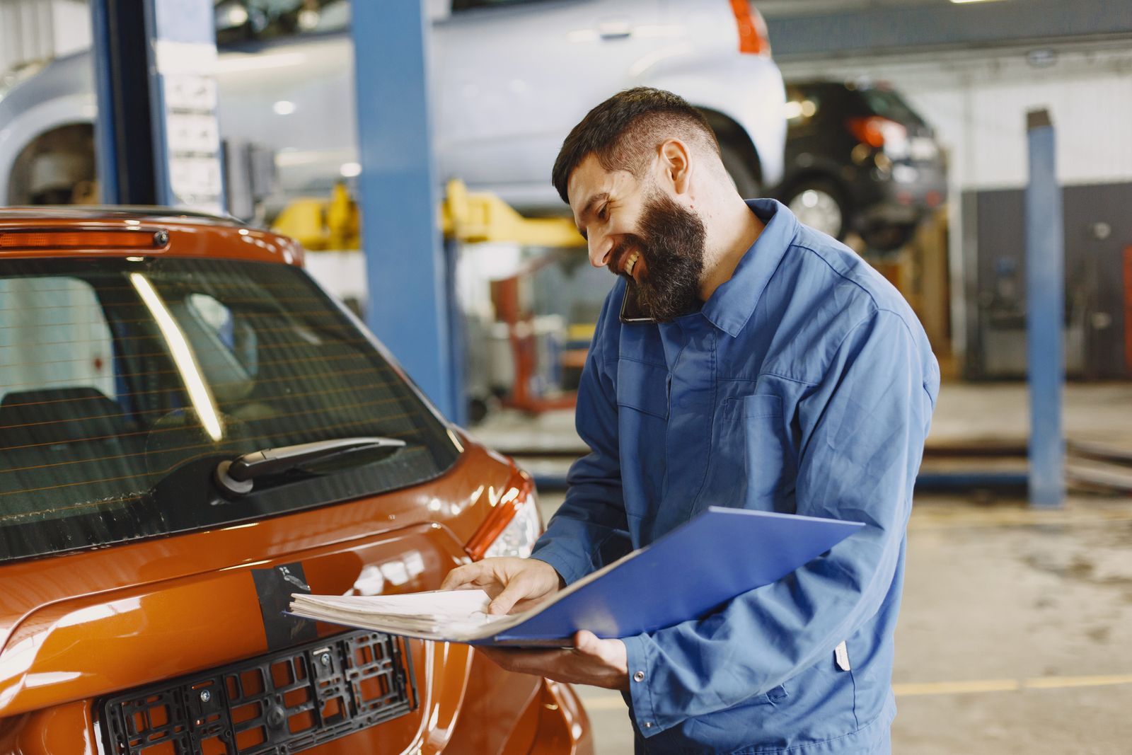 A smiling mechanic reviews paperwork on the phone beside a customer's car in a repair shop — illustrative stock photo, not a photo of Brazos Valley Automotive or its staff.