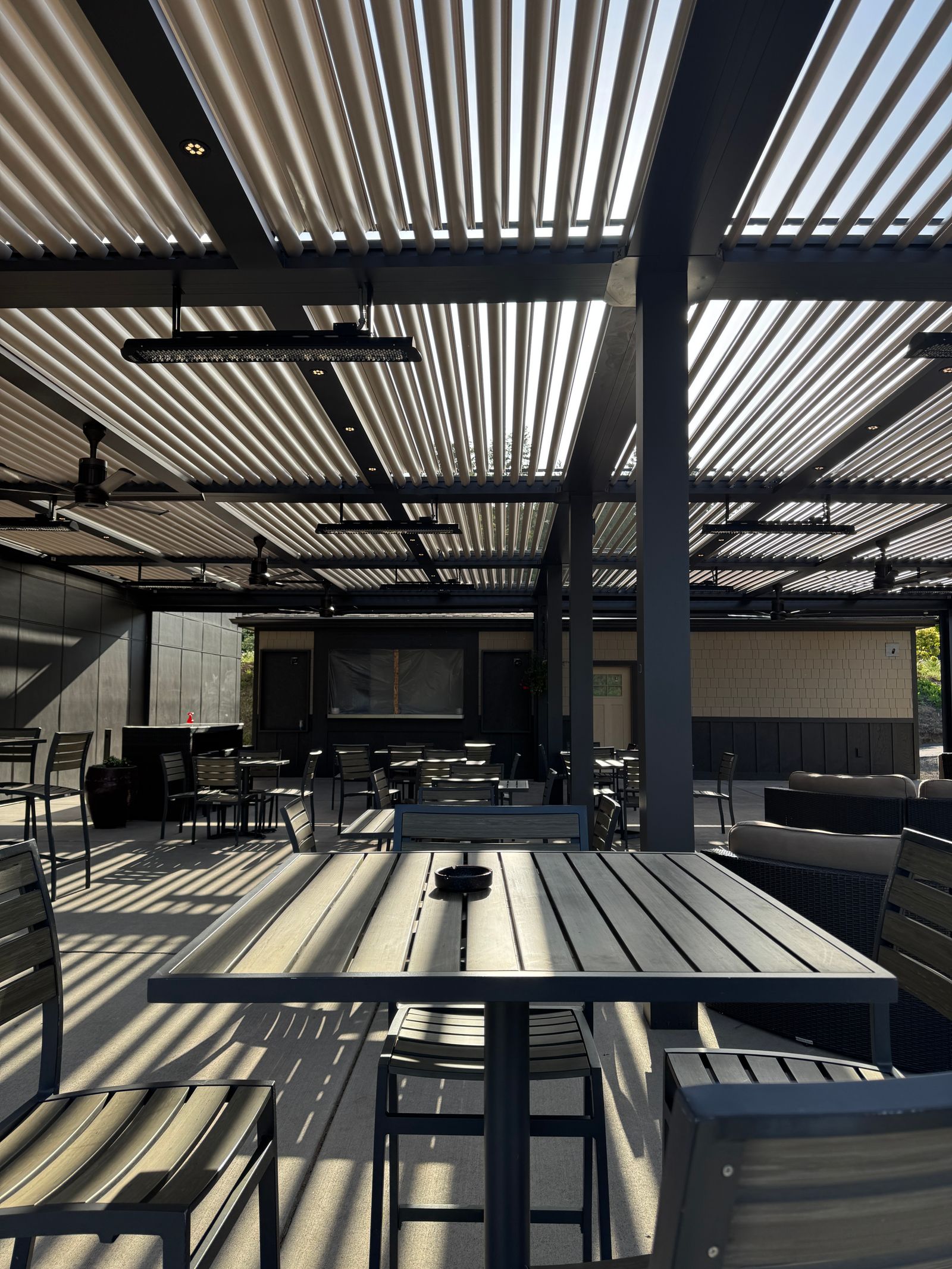 A modern outdoor patio with metal furniture under a slatted aluminum pergola roof — illustrative stock photo, not a photo of a Bryan Awnings installation.