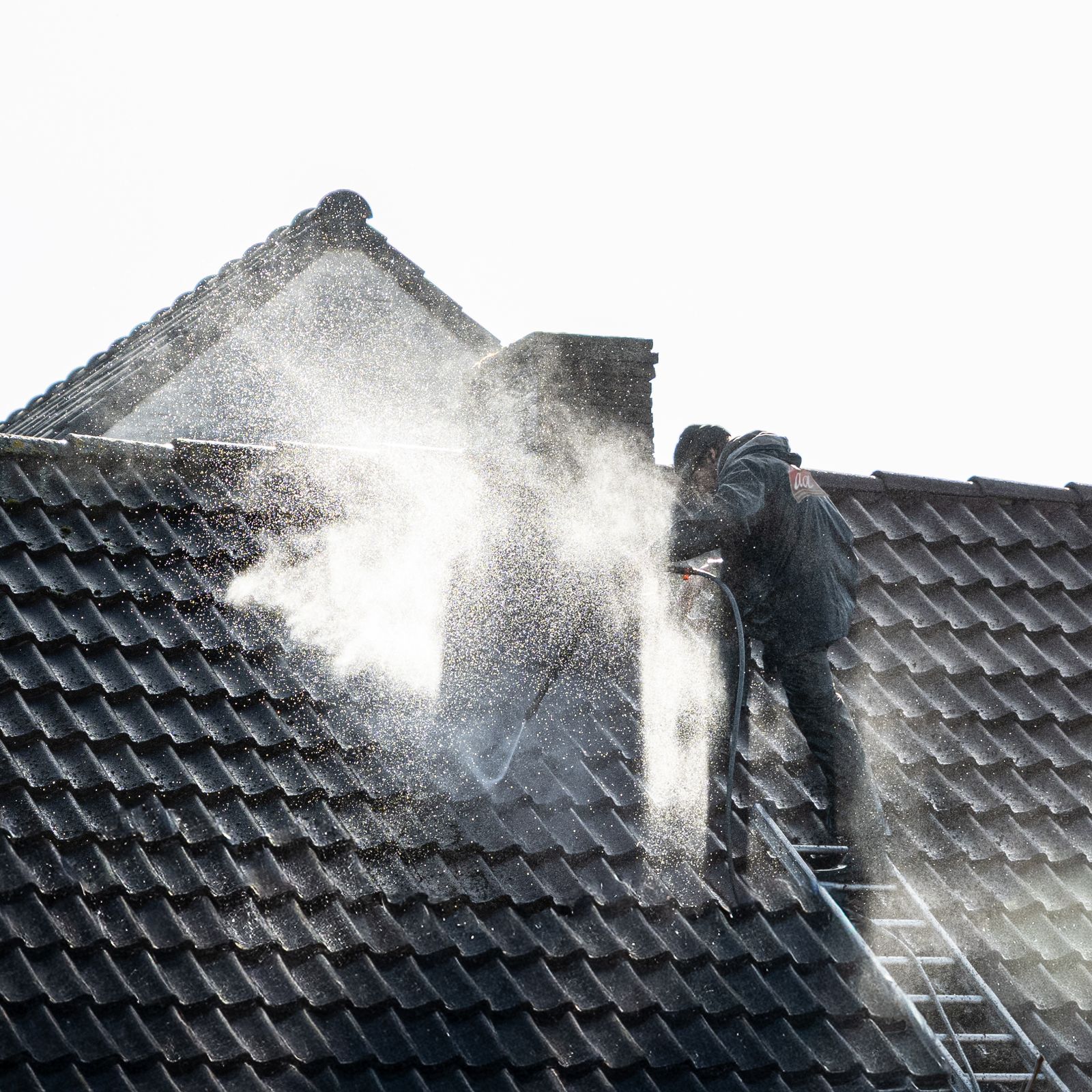 A worker power washing roof tiles, removing grime and buildup — illustrative stock photo, not a photo of Bucket of Suds or its crew.