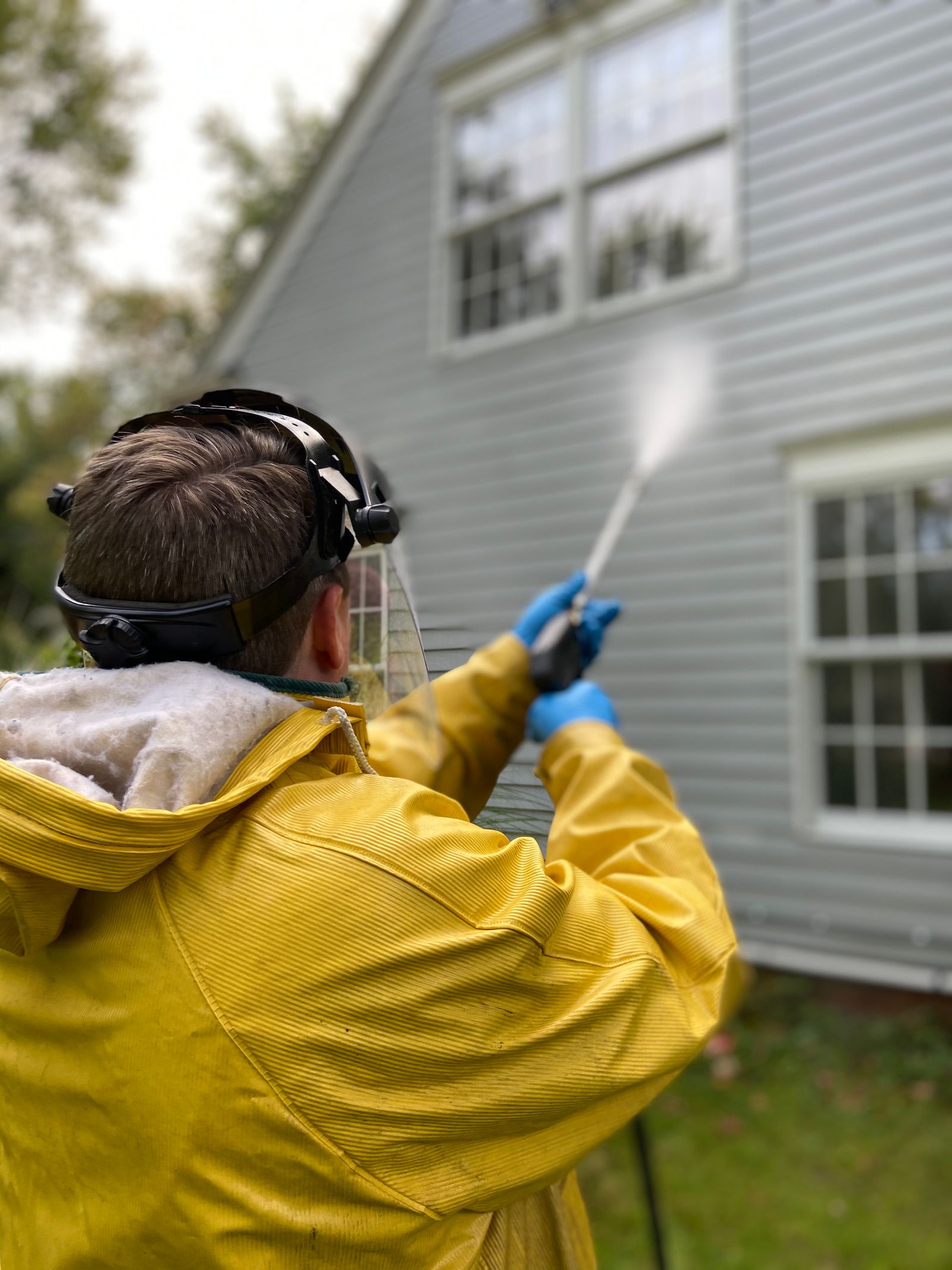 A person cleaning house siding with a pressure washer, wearing protective gear — illustrative stock photo, not a photo of Bucket of Suds or its crew.