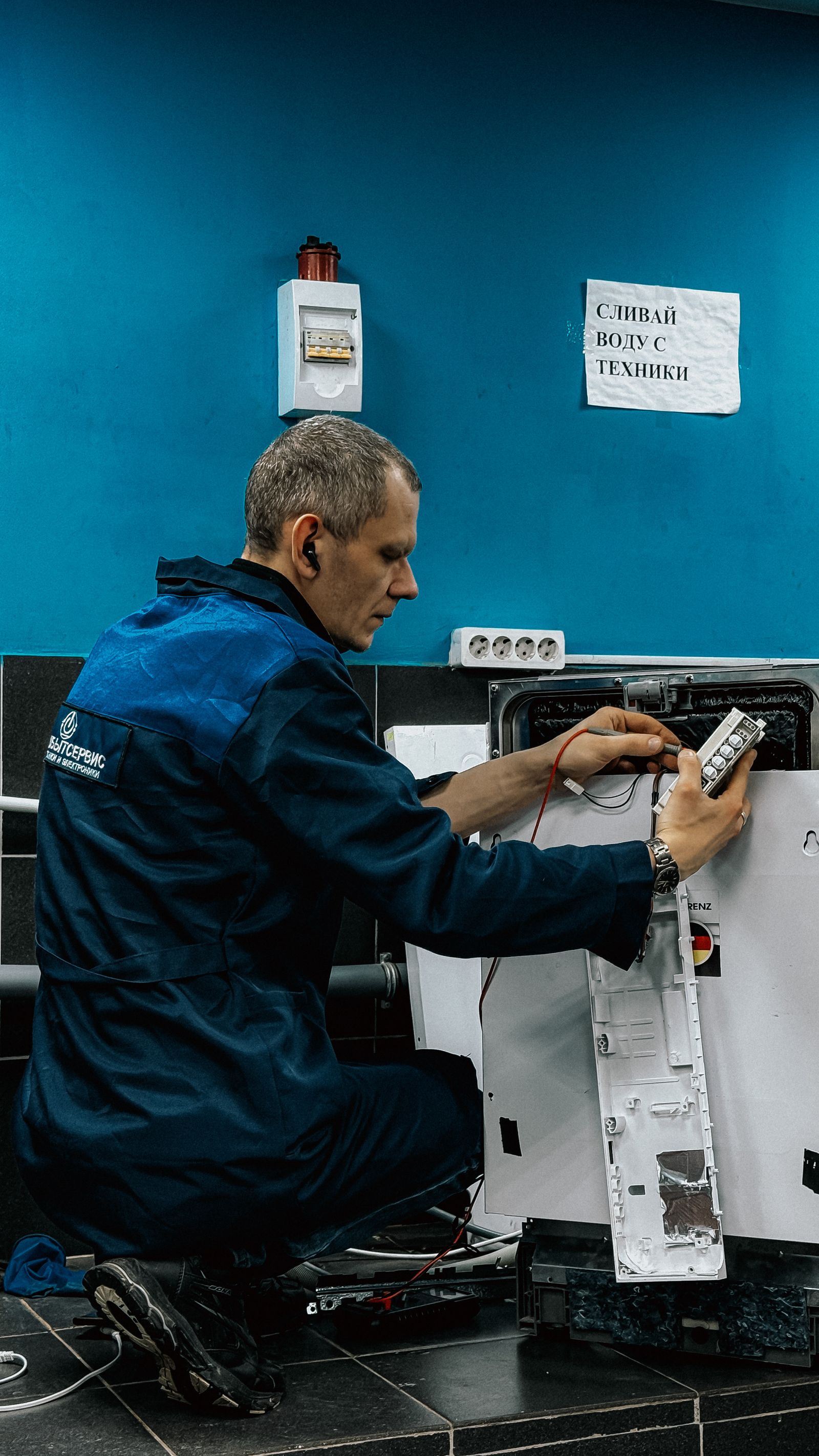 A technician in a blue uniform focused on repairing a home appliance indoors — illustrative stock photo, not a photo of Norman Bush or Bush's Appliance Repair.