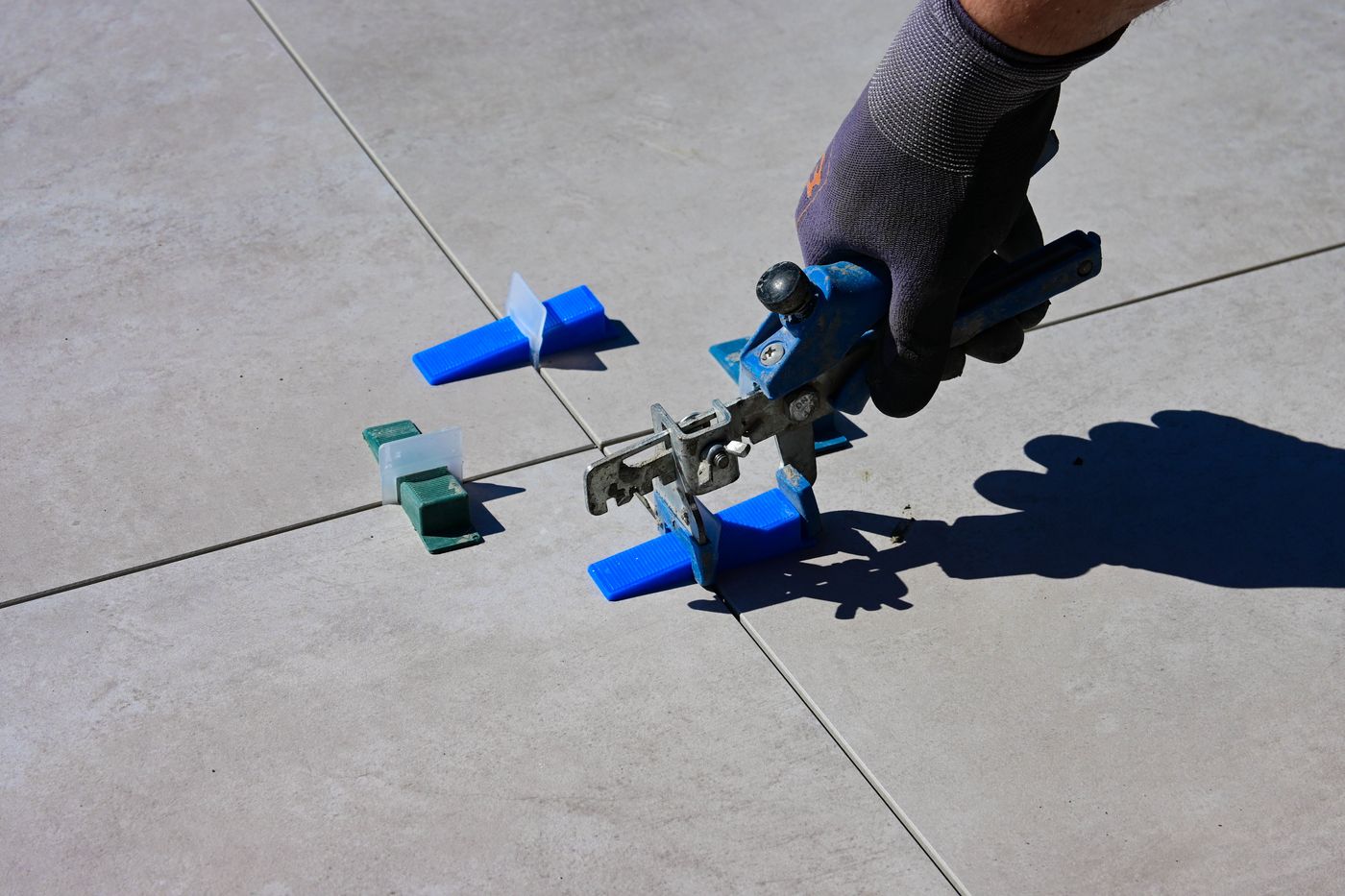 Gloved hand using a tile-leveling tool during installation, illustrative stock photo