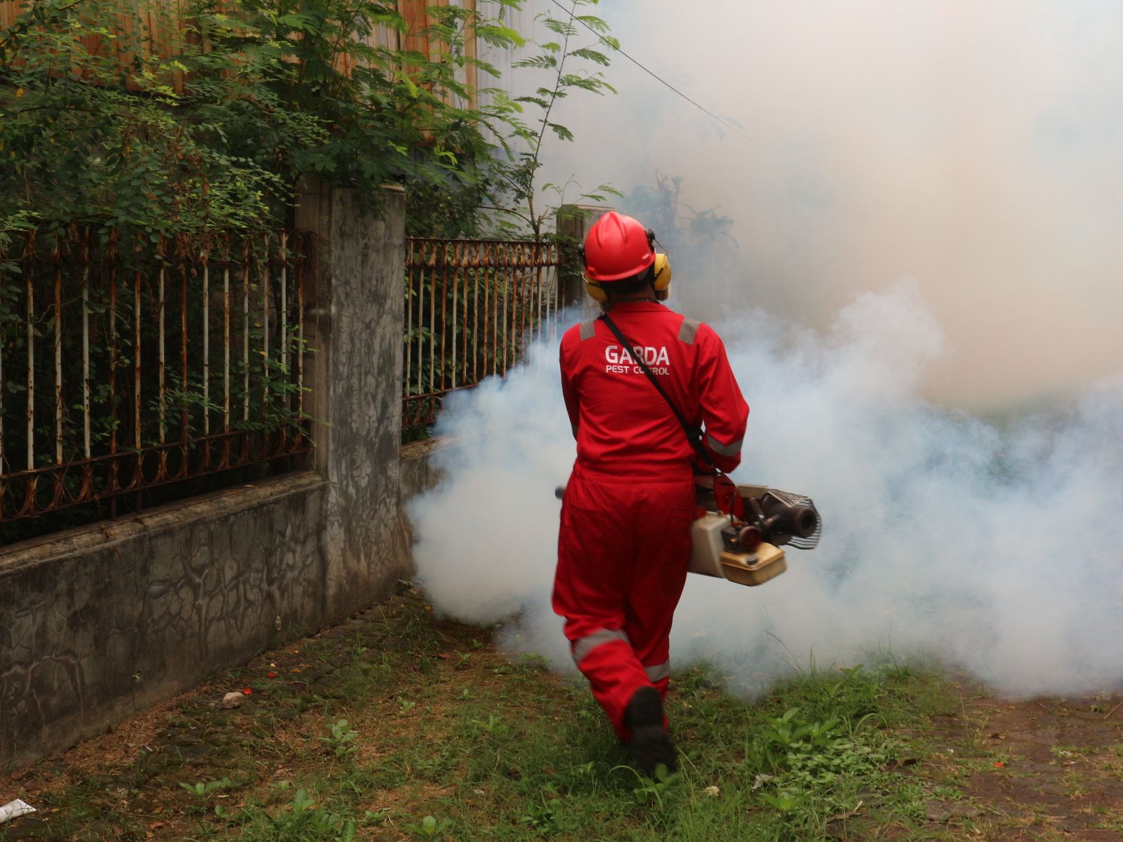 A pest control technician in a red uniform treating an outdoor residential yard with fogging equipment — illustrative stock photo, not a photo of Dan or Danomite's own work.