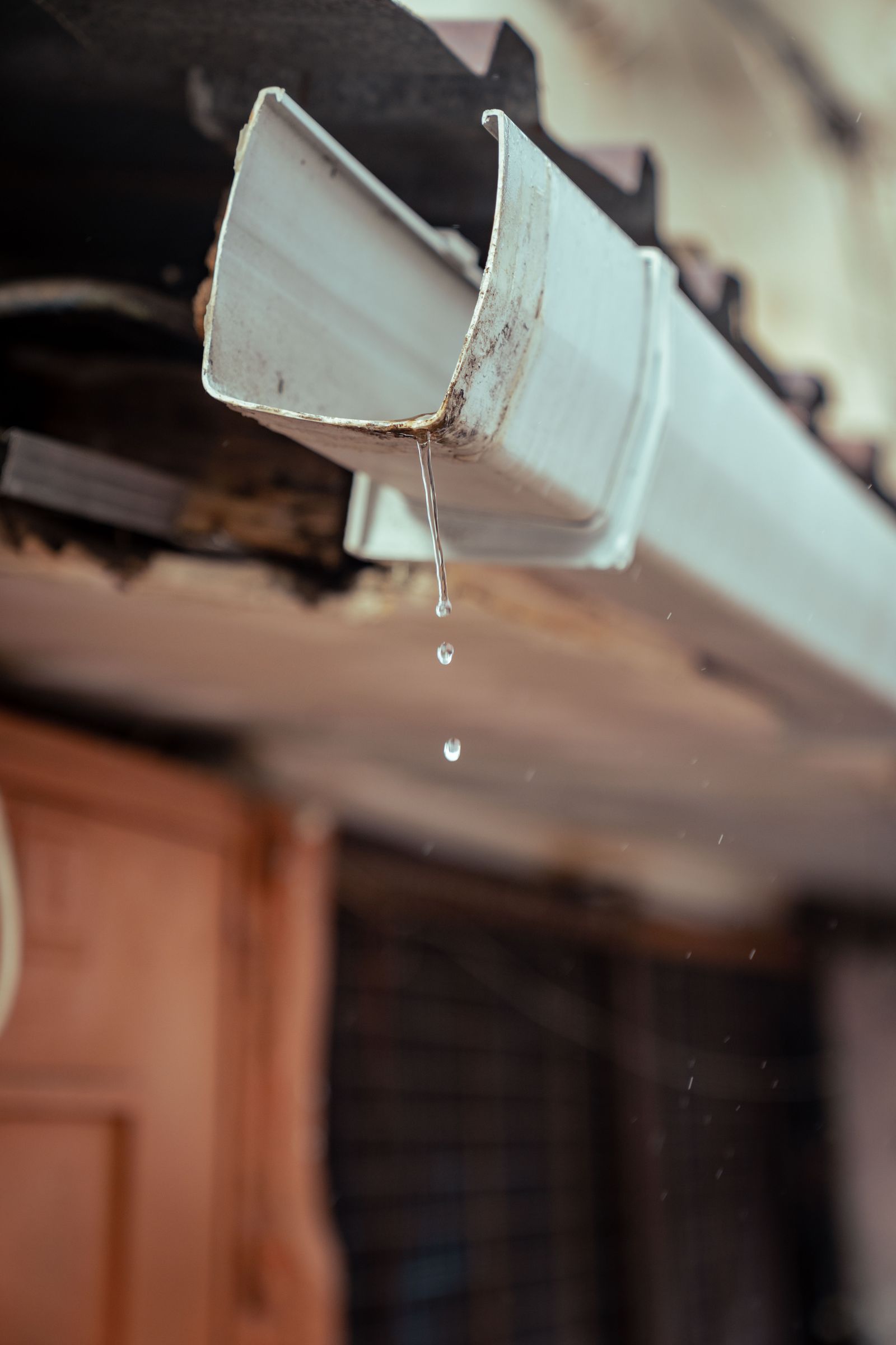 Detailed shot of rainwater droplets falling from a house gutter — illustrative stock photo, not a photo of DC Custom Seamless Gutters' work.