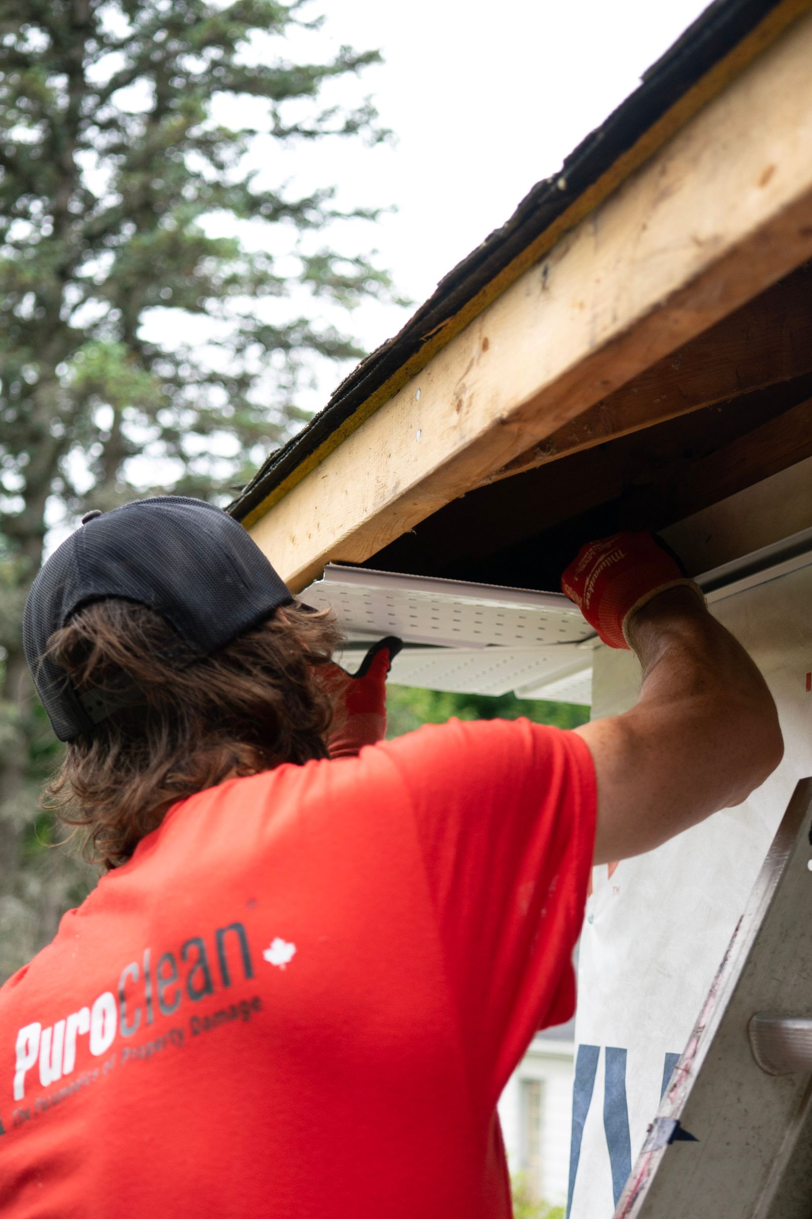 A construction worker installing a gutter under a wooden roof, focusing on precision — illustrative stock photo, not a photo of DC Custom Seamless Gutters or its crew.