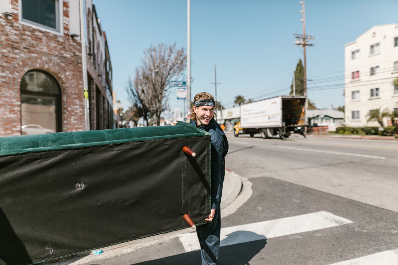 A man carrying a couch across a sunny urban street during a haul-away job — illustrative stock photo, not a photo of Feral's own crew or a Feral job site.