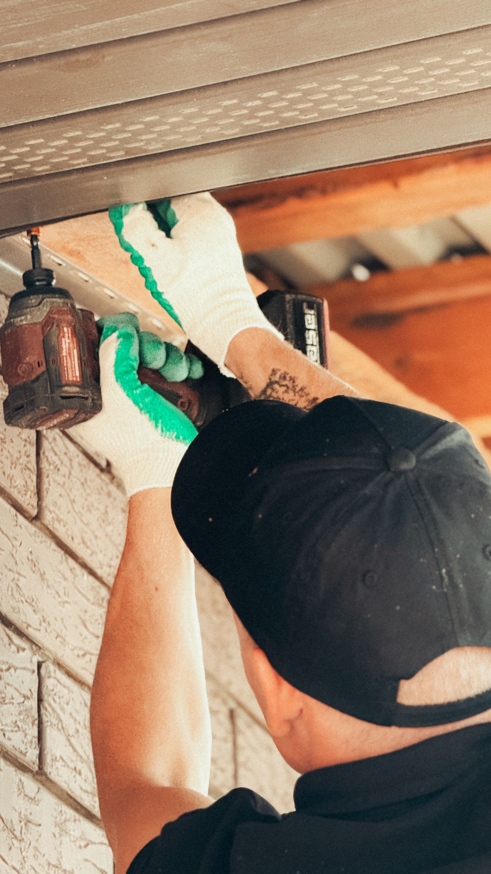 A handyman installing an outdoor light fixture under a roof overhang with a cordless drill — illustrative stock photo, not a photo of Larry or his work.