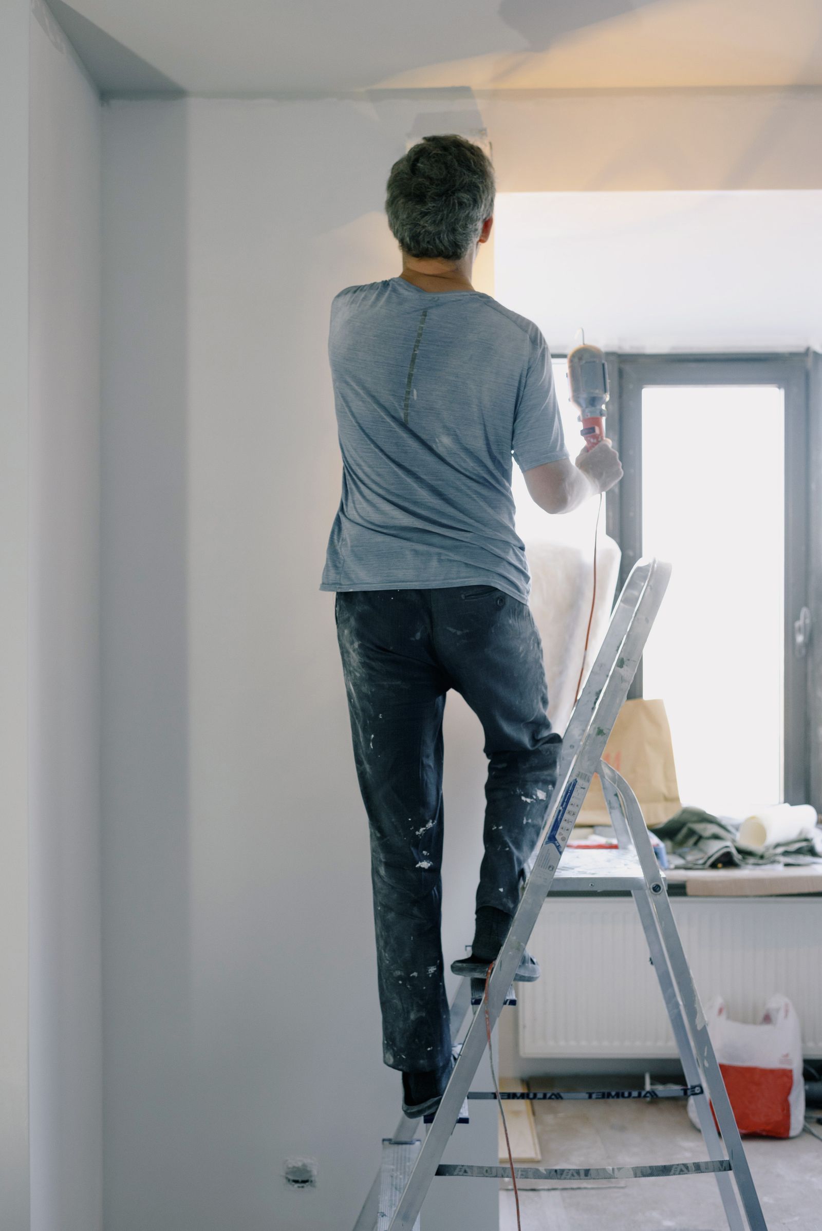 A handyman on a ladder using a power tool for a home renovation task indoors — illustrative stock photo, not a photo of Larry or his work.