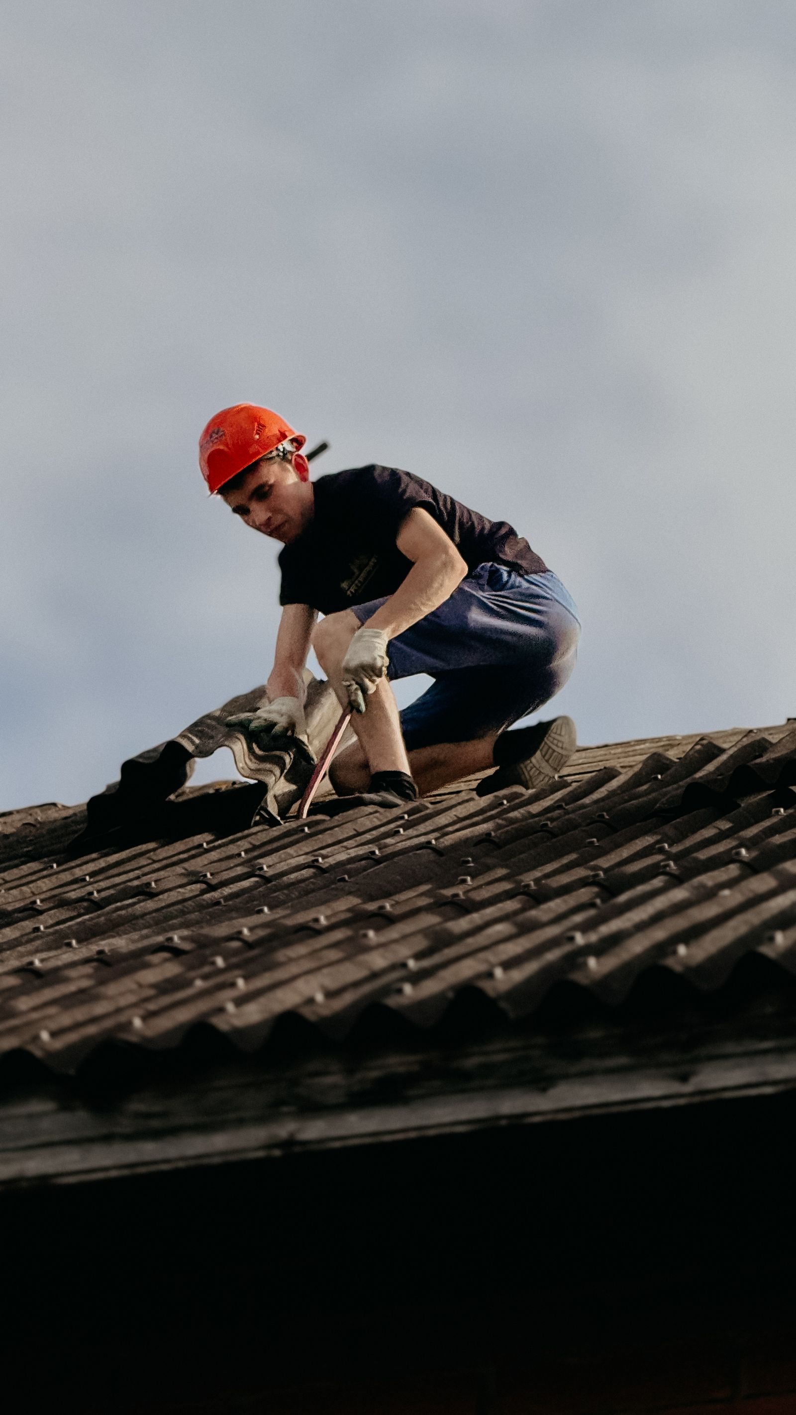 A construction worker with a safety helmet repairing a residential brick house roof in daylight — illustrative stock photo, not Lopez Roofing's own crew.