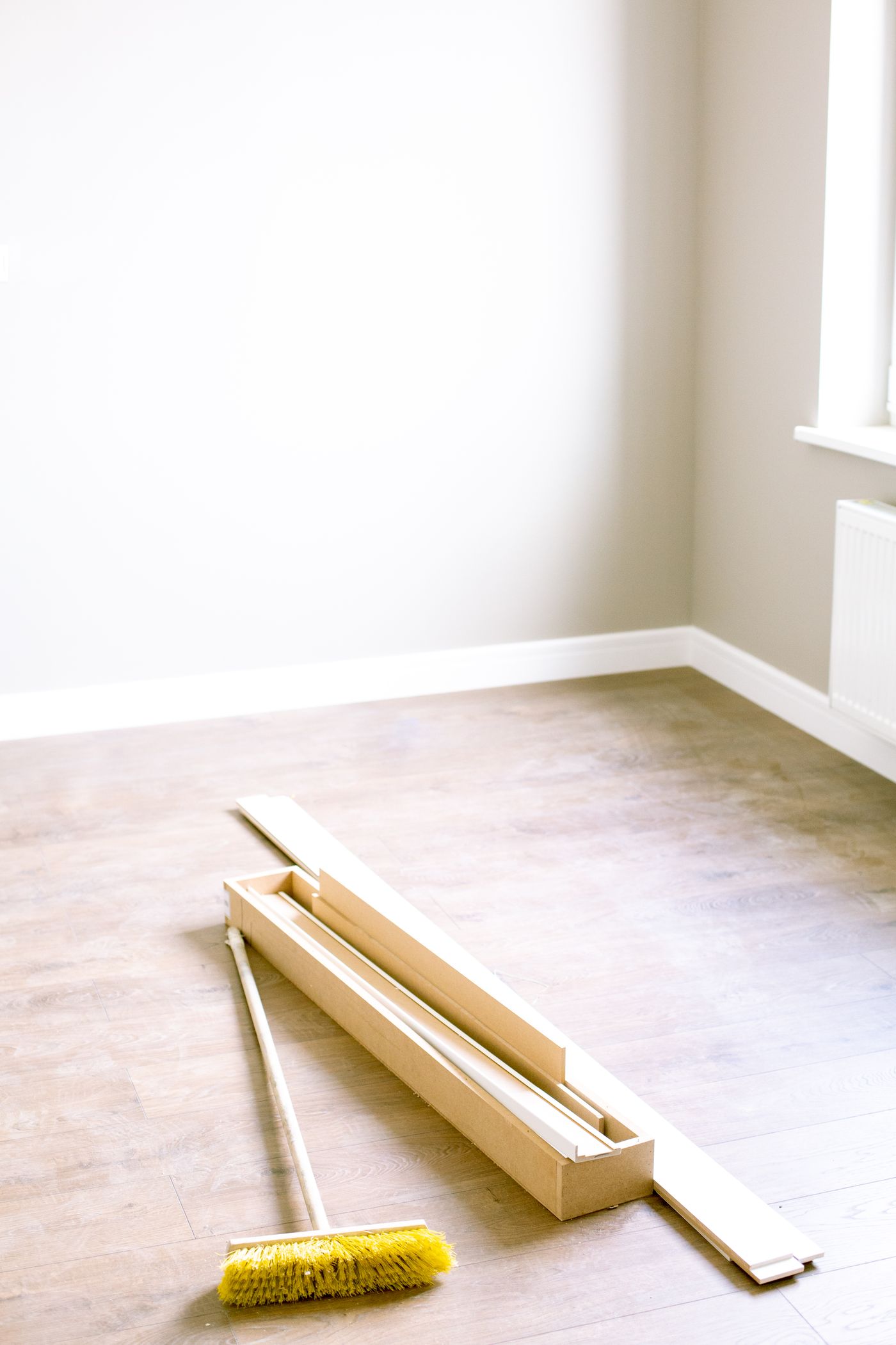 Empty room prepped with wood planks and a broom, ready for flooring installation, illustrative stock photo