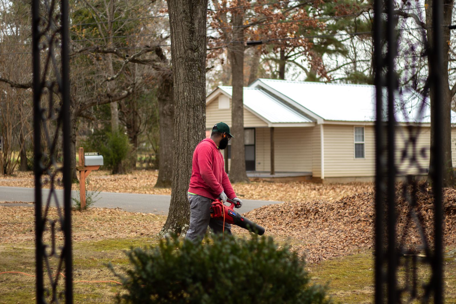 A landscaper using a leaf blower in a rural yard with bare trees and a small house in the background — illustrative stock photo, not a photo of Mike's Complete Tree Services and Landscaping or its crew.