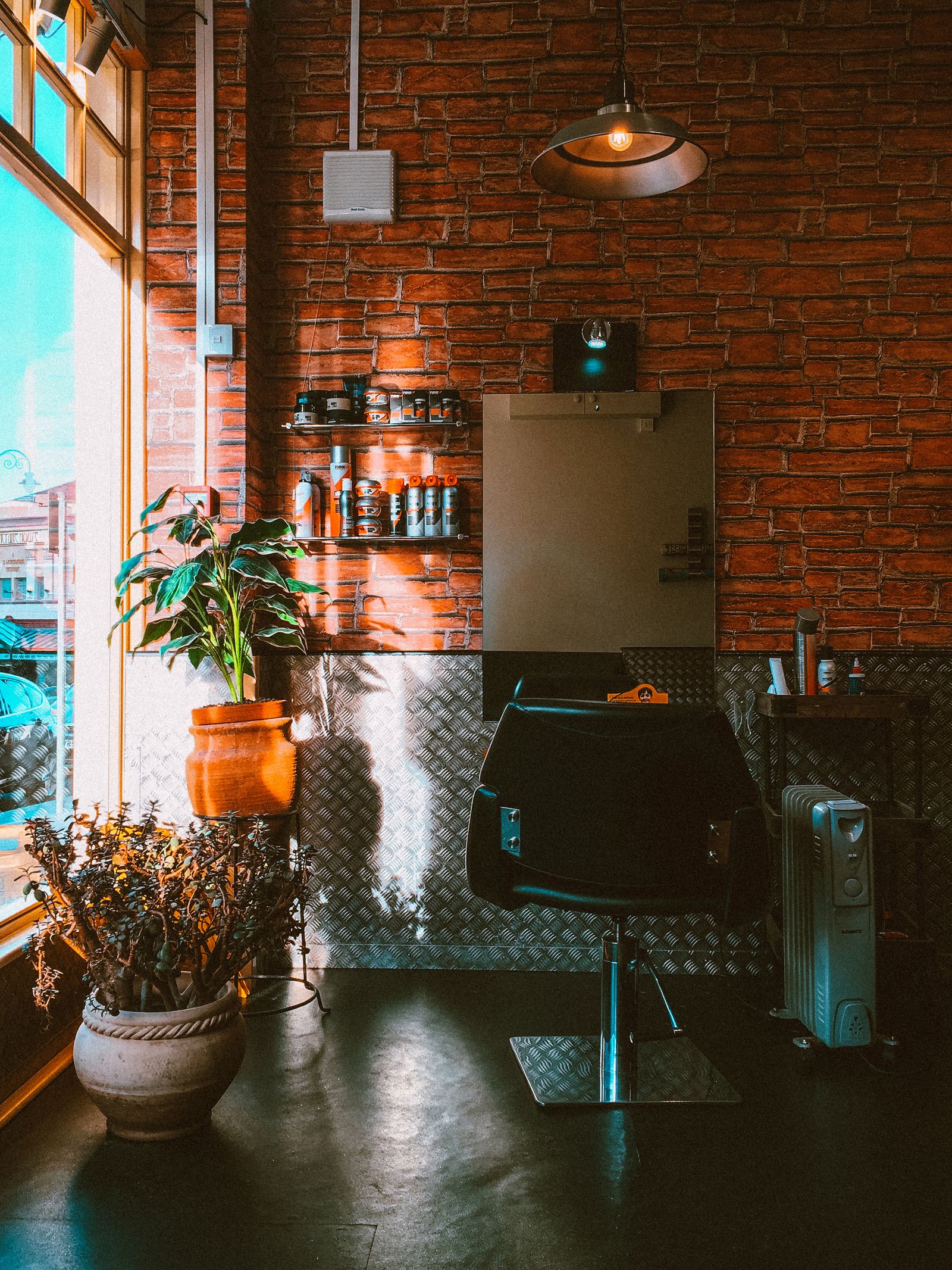A warm, industrial-style barbershop interior with exposed brick, a barber chair, and styling products on a shelf — illustrative stock photo, not a photo of Neff's Majestic Hair Studio.