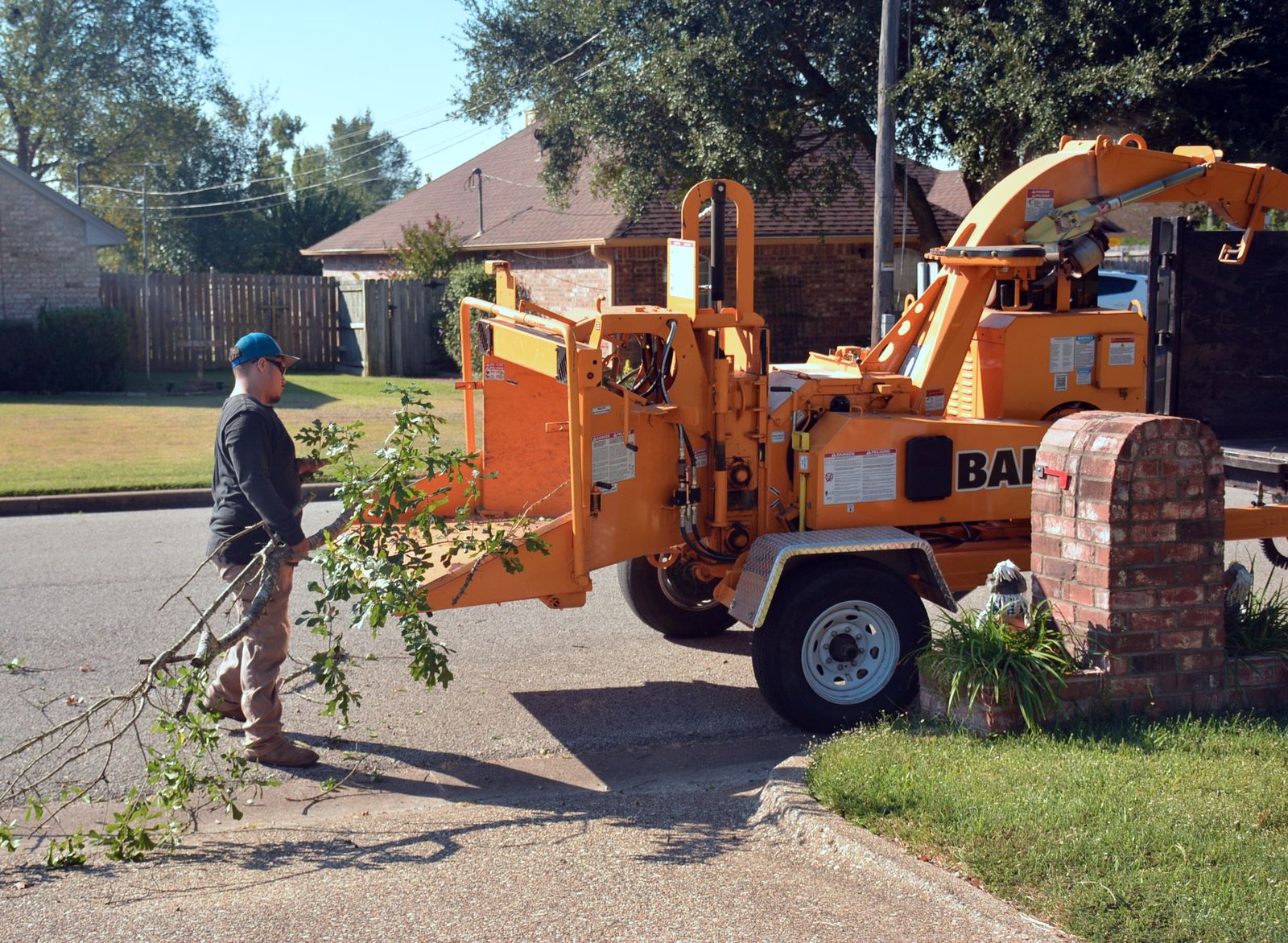 A worker feeding cut branches into a wood chipper on a residential street with brick homes nearby — illustrative stock photo, not a photo of Pete's Trees or its crew.
