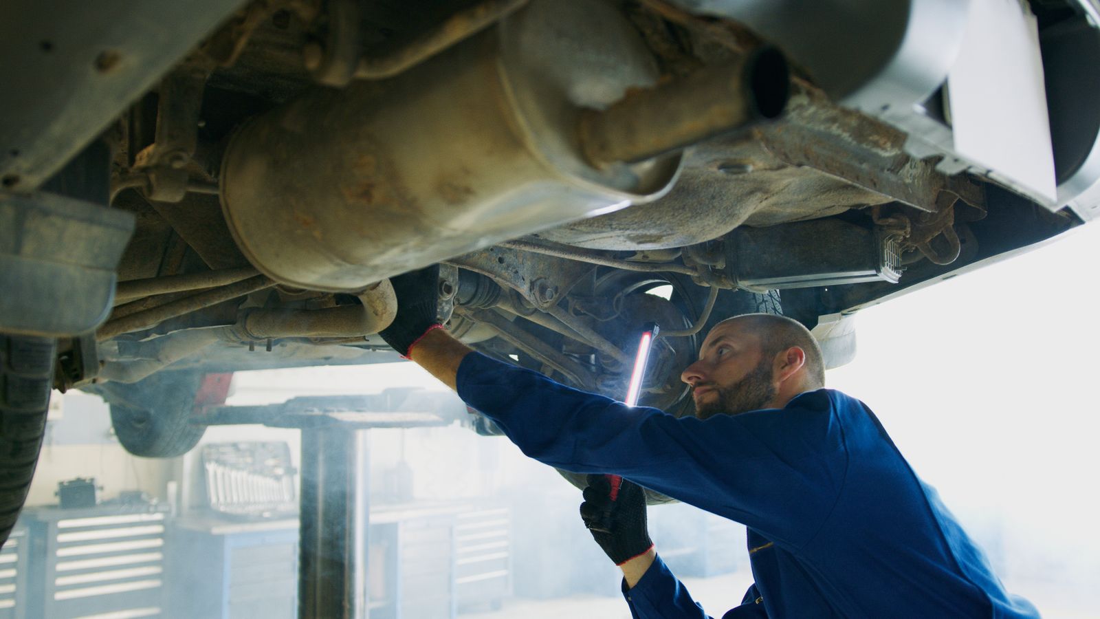 A mechanic in coveralls performing maintenance underneath a vehicle in a garage — illustrative stock photo, not a photo of Soto's Mufflers or its staff.