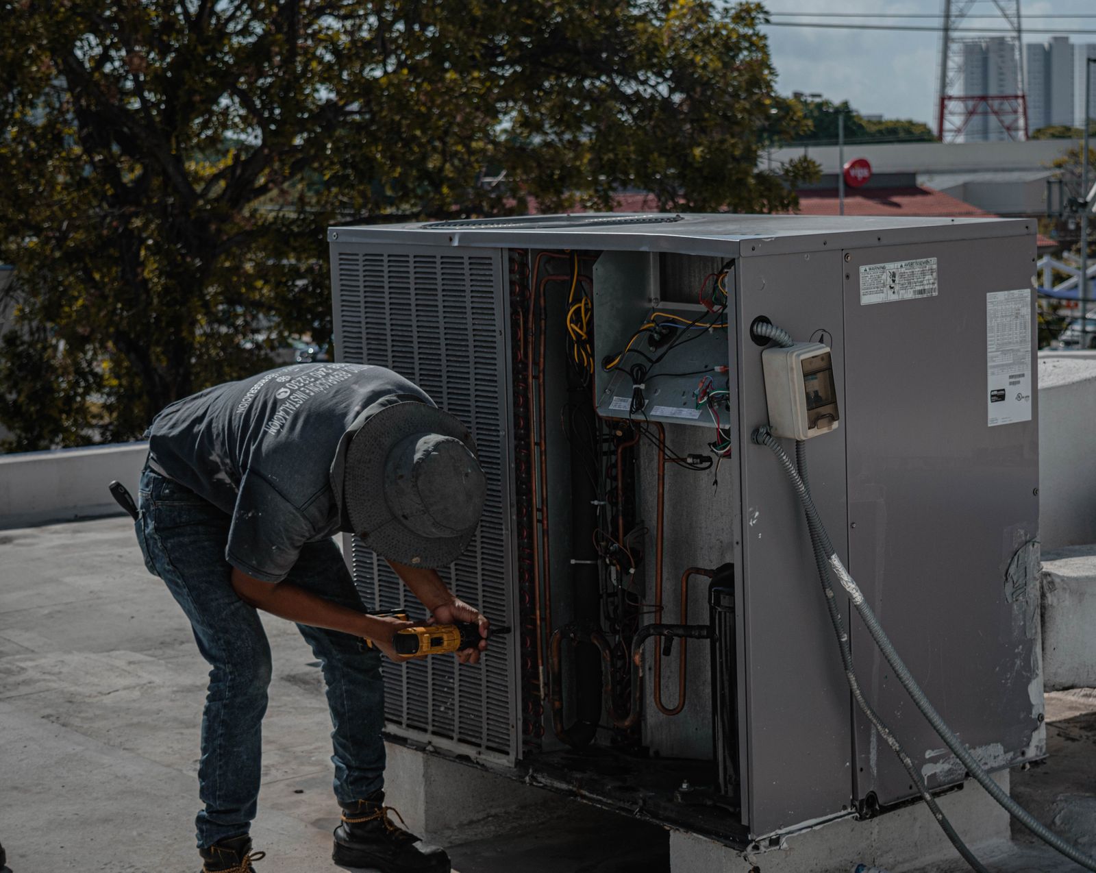 An HVAC technician servicing an open outdoor condenser unit on a rooftop, tools in hand — illustrative stock photo, not a photo of Static Heating and Air Conditioning or its staff.