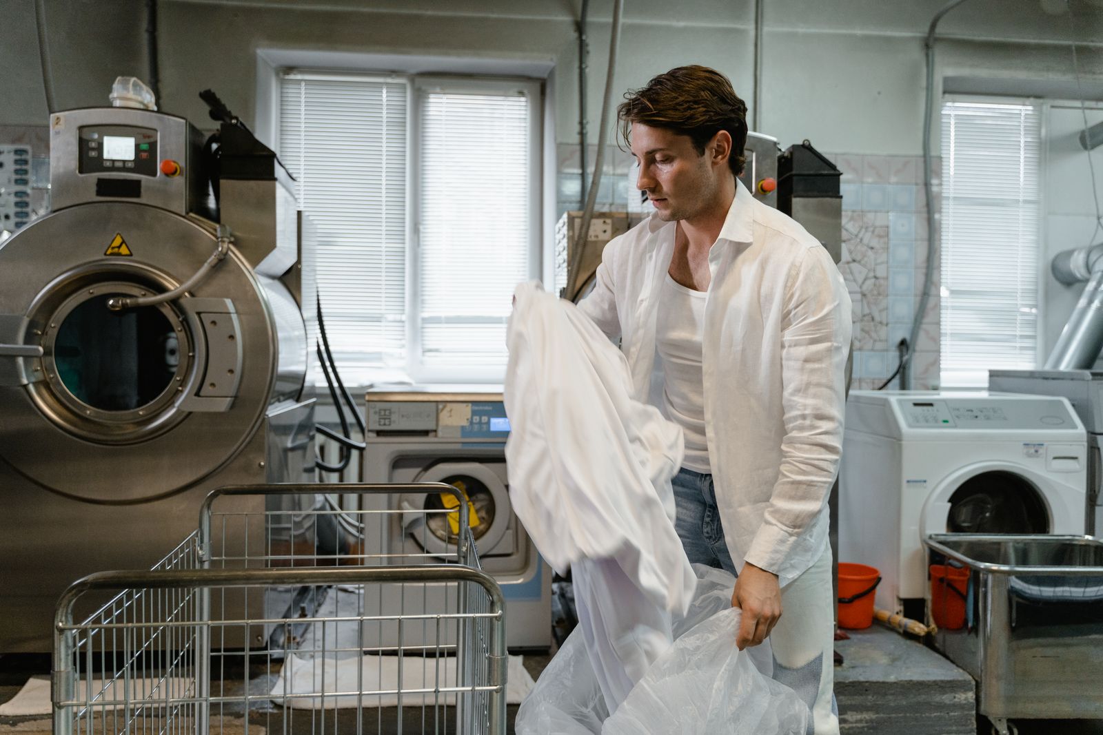 A worker organizing pressed laundry in a clean commercial facility with industrial machines — illustrative stock photo, not a photo of West 25th Laundry & Dry Clean or its staff.