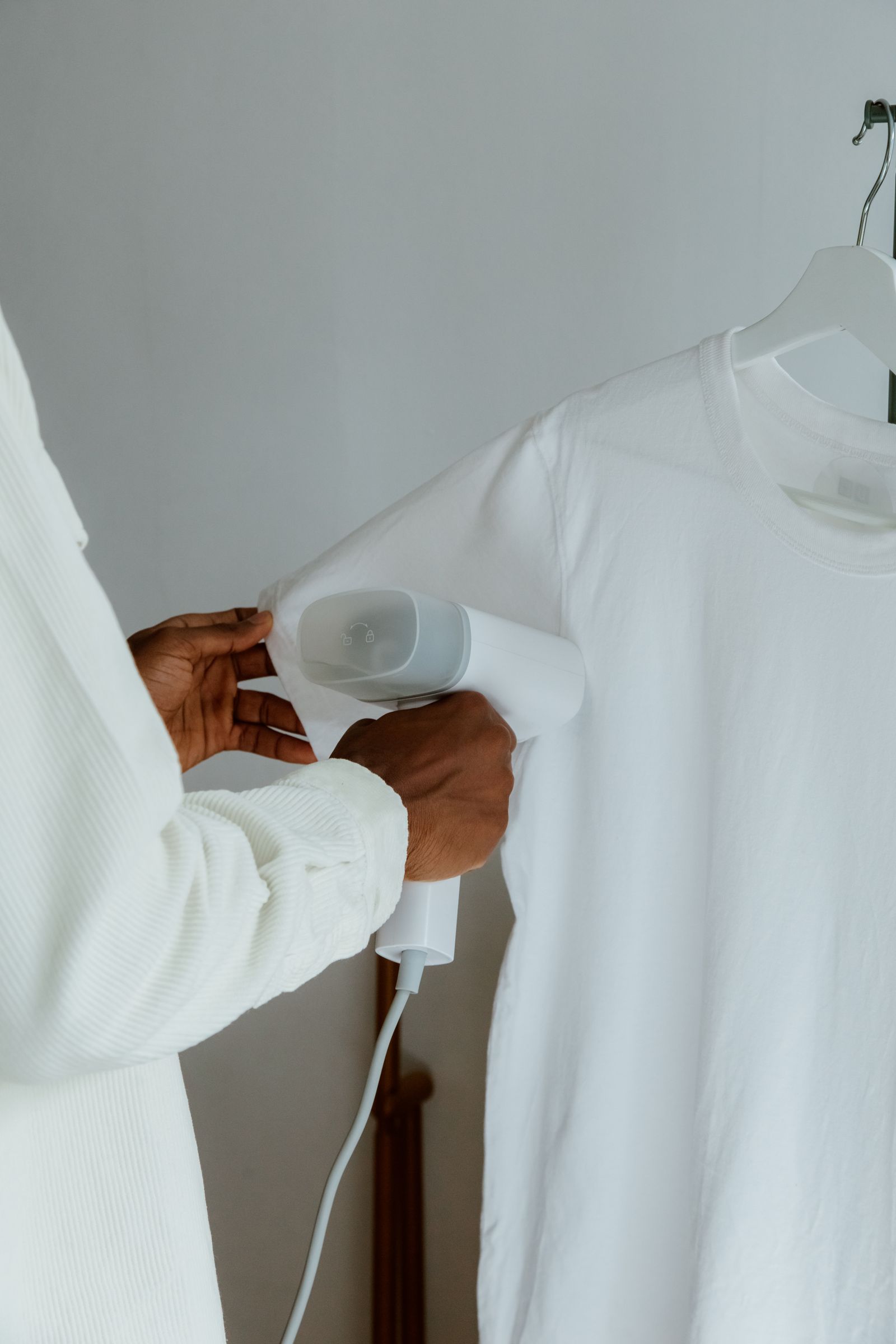 Hands using a steam iron to press a white shirt hanging indoors — illustrative stock photo, not a photo of West 25th Laundry & Dry Clean.